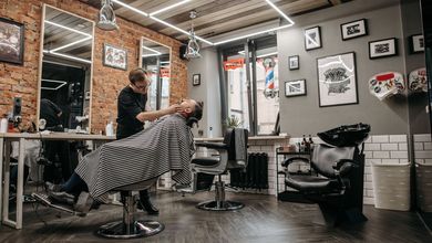 Barbero arreglando la barba a un cliente reclinado en el sillón