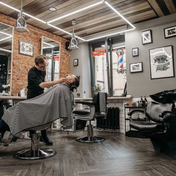 Barbero arreglando la barba a un cliente reclinado en el sillón