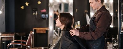 Curso de Peluquería unisex: peluquera preparando a una clienta con capa en el sillón